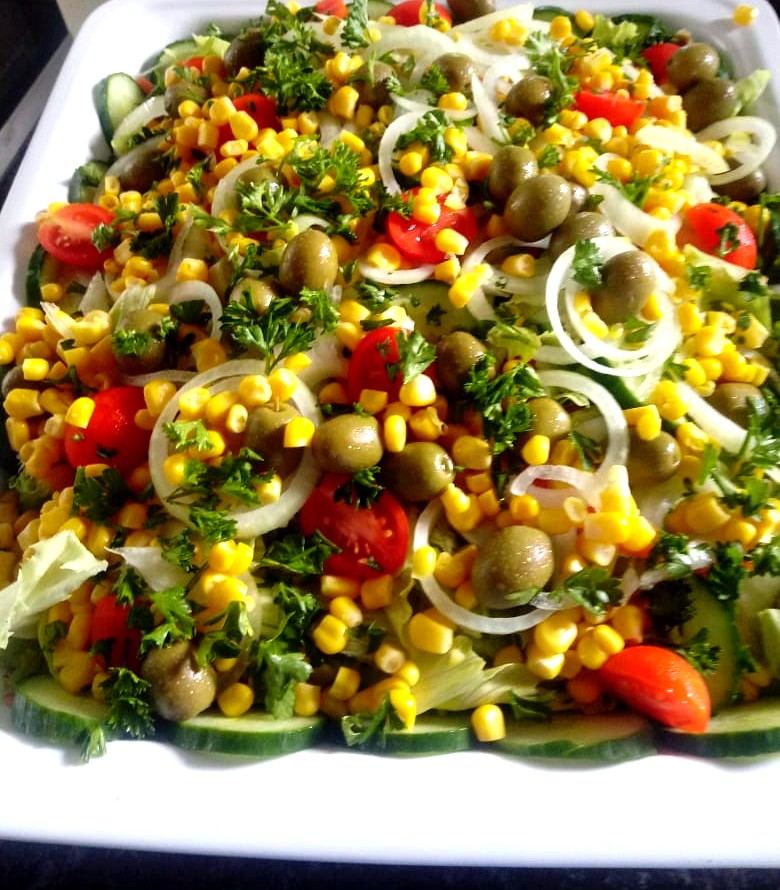 Salad of sweetcorn, green olives, tomato, onion rings and parsley on cucumber slices