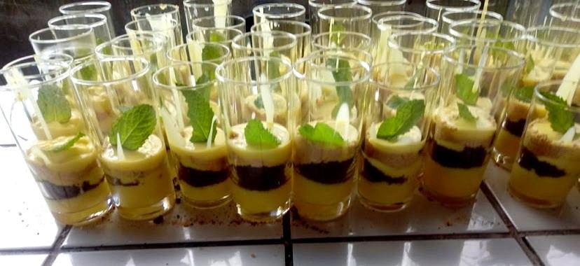 Rows of dessert shooters layered with custard and dark crumb, topped with fresh mint