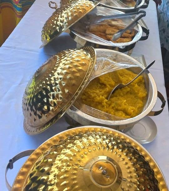 Hammered gold lidded serving dishes holding pap and fried chicken on a white tablecloth
